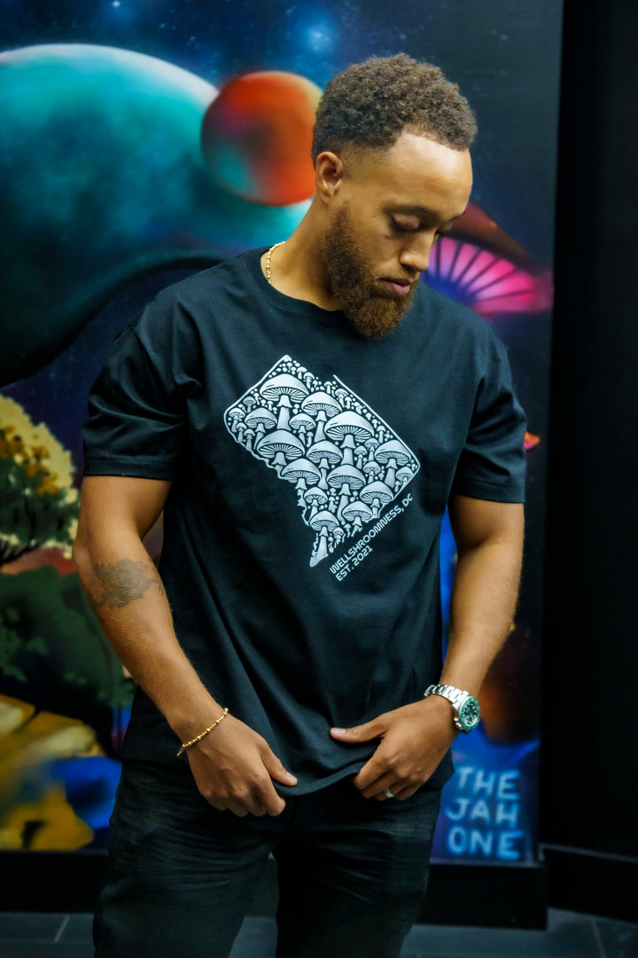 Wellshroomness DC Heavyweight Tee in black worn by a man standing in front of a mural in a city