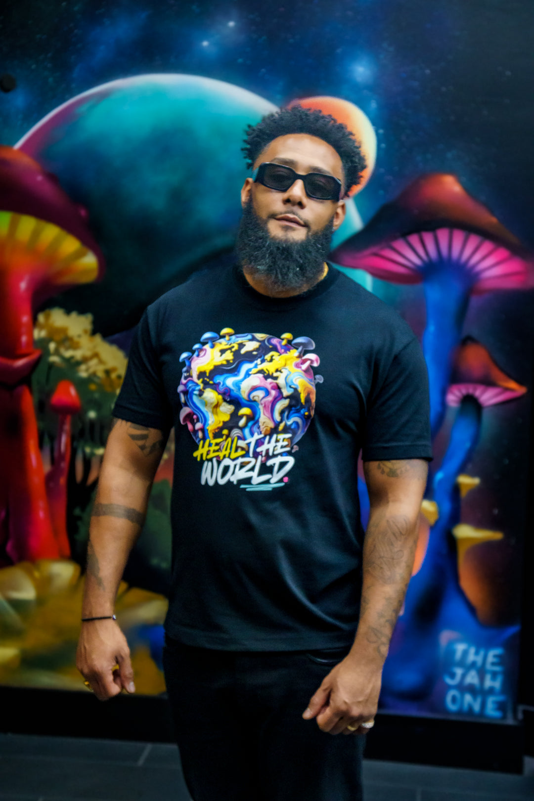 Heal the World Heavyweight Tee in black worn by a man standing in front of a mural